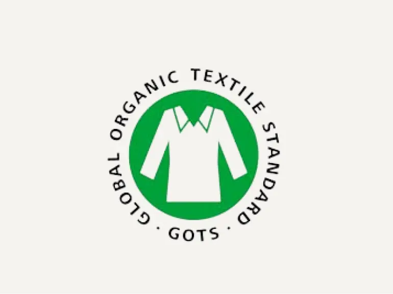 Logo des Global Organic Textile Standard (GOTS) mit einem weißen Hemdsymbol auf einem grünen Kreis, umgeben vom Text GLOBAL ORGANIC TEXTILE STANDARD GOTS.