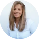 Eine Frau mit langen blonden Haaren und einem weißen Hemd mit Knöpfen lächelt vor einem schlichten weißen Hintergrund.